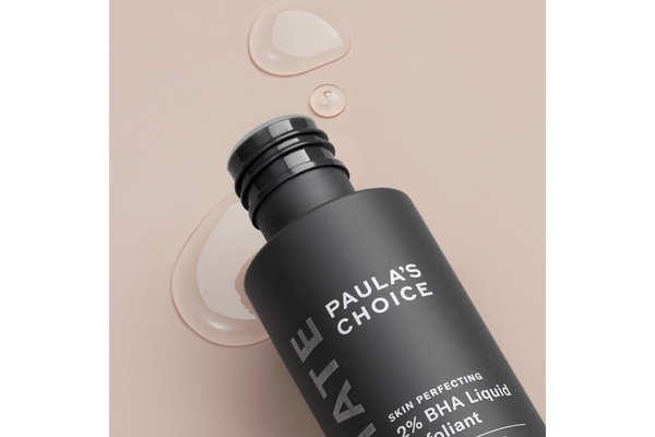 Image Paula's Choice BHA liquid on its side with some of it spilling out on a pink background.